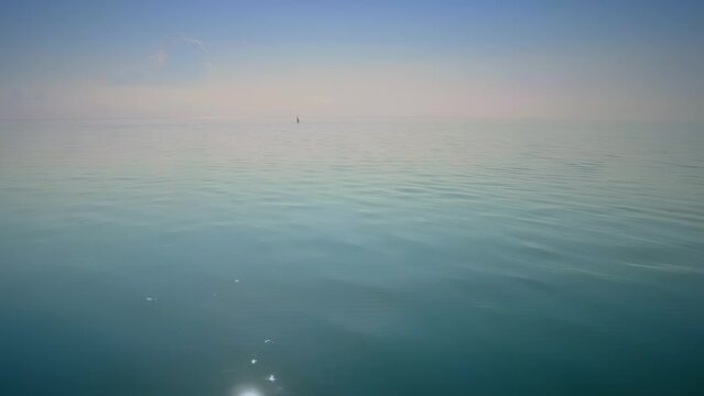 Small yacht sailing in a calm distant dreamy ocean on a sunny day. First Encounter Beach, Cape Cod, Massachusetts, United States of America.