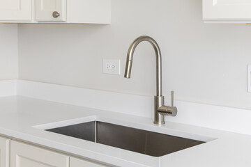A kitchen sink detail with a polished chrome faucet, white marble countertop, and white cabinets.