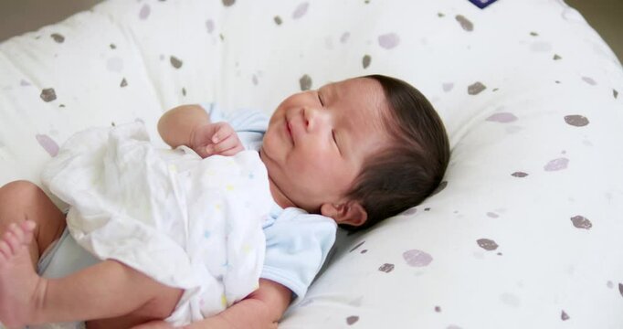 Wearing a piece of blue onesie and in his diapers, a baby is stretching out its hands and legs as it lies on its crib.
