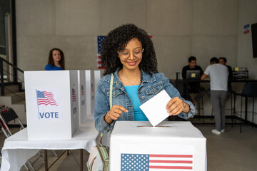 portrait of a young african american woman voting in the us election, placing vote ballot in the...