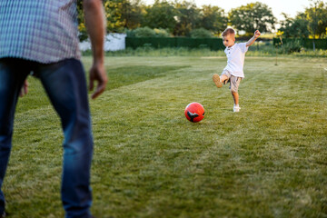 Playful little boy kicking a soccer ball and playing game with granddad in backyard.