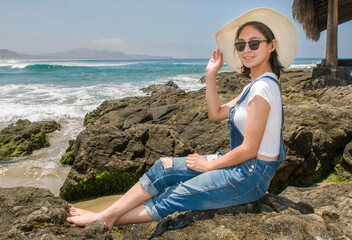 A young Hispanic Mexican girl enjoying her vacation sitting on the rocks on a beach in Todos Santos, Baja California Sur. MEXICO, with mountains and the Pacific Ocean waves in the background.