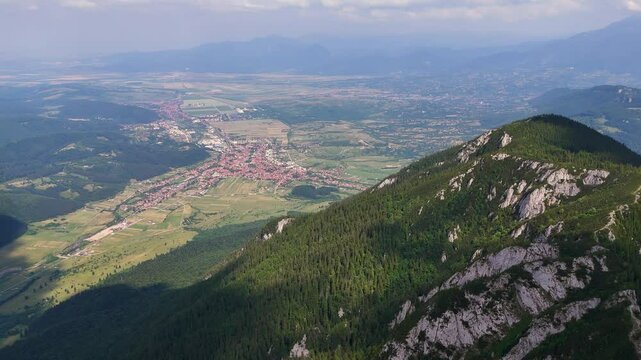 Drone moves forward, revealing Zarnesti city and Piatra Mica peak
