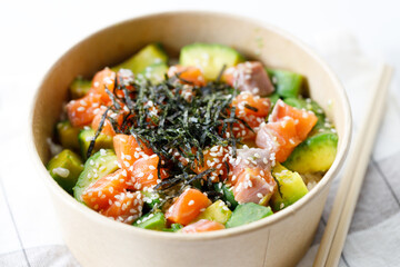 poke bowl with diced raw salmon fish and avocado on sushi rice in paper container.