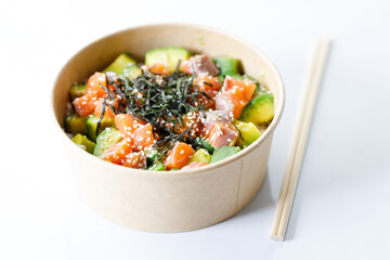 poke bowl with diced raw salmon fish and avocado on sushi rice in paper container.