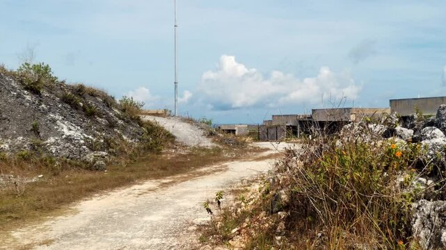 Steady hot of a gravel road in a wasteland. Deserted unfinished houses in a post-apocalyptic atmosphere. Ideal for projects needing a desolate wasteland landscape. Recorded in bright sunlight at 3pm.