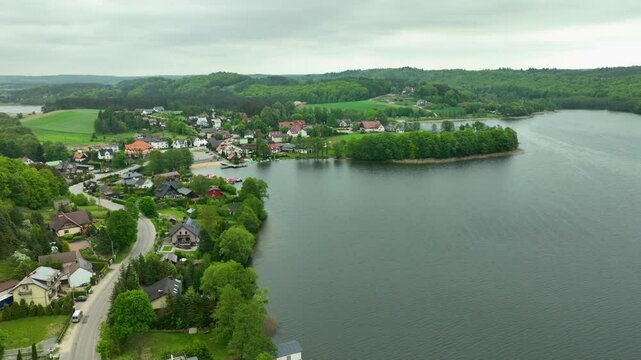 Aerial view of a quaint village by a lake with lush green surroundings and scattered houses - Ostrzyce