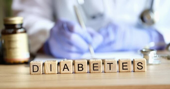 Doctor endocrinologist writing out prescription on background of wooden cubes with word diabetes closeup 4k movie. Diagnosis and treatment of diabetes mellitus concept
