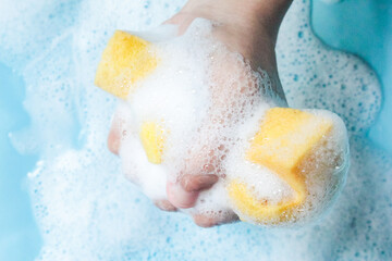 hand squeezing a foamy sponge, on a blue background