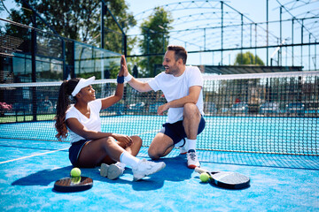 Happy athletic couple giving high-five while playing paddle tennis on court.