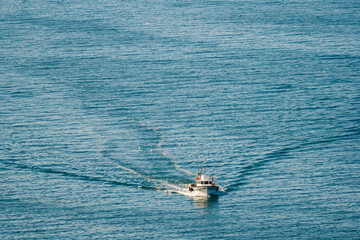 Naklejka premium Small boat sailing on a calm blue sea, leaving a trail of waves behind, in Turkey.