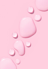 round drops of transparent gel serum on pink background