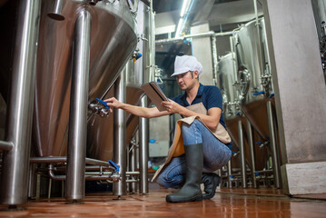 Fototapeta premium Asian man works at a craft beer factory as a brewer operating the brewery machinery. Craft beer production is a small business.