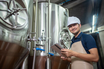 Asian man works at a craft beer factory as a brewer operating the brewery machinery. Craft beer production is a small business.