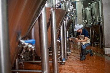 Asian man works at a craft beer factory as a brewer operating the brewery machinery. Craft beer production is a small business.