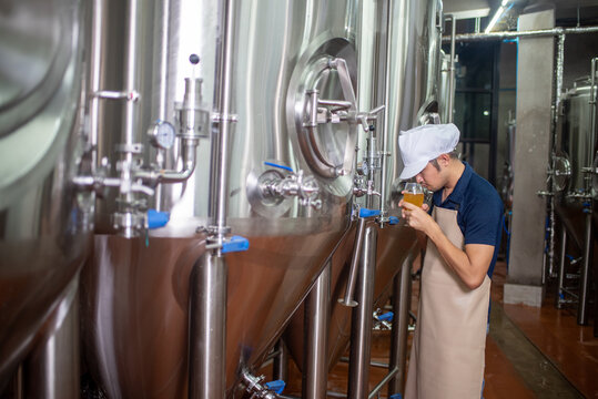 An Asian male brewer tests beer samples by pouring beer