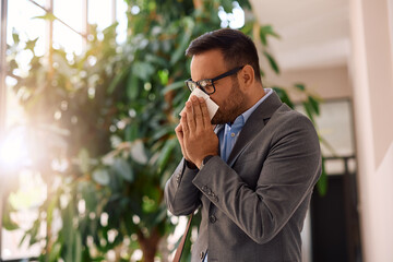 Sick businessman sneezing into  tissue in office.