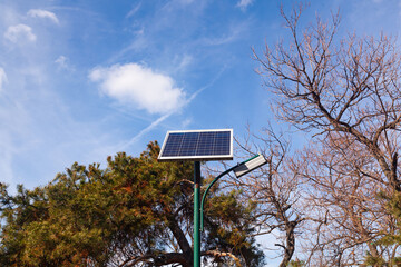 A solar panel is installed on a street lamp post in a park.