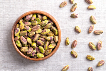 Pistachios kernels, roasted and salted nuts in a wooden bowl on linen fabric. Shelled and crunchy toasted fruits of Pistacia vera. Ready-to-eat snack food. Close-up from above, food photo.
