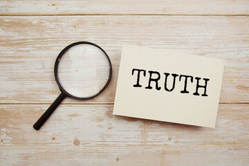 Truth text written on papercard with magnifying glass on wooden background