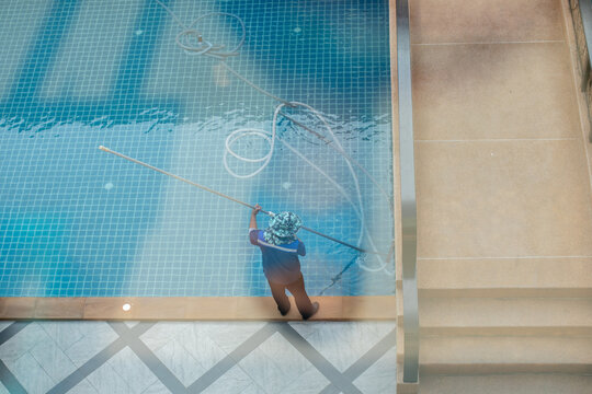 Staff are cleaning the hotel pool using an underwater vacuum pump.