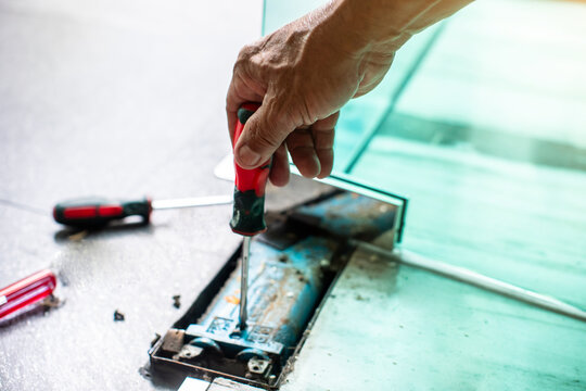An interior decorator uses a screwdriver to adjust the angle of a swinging glass door.