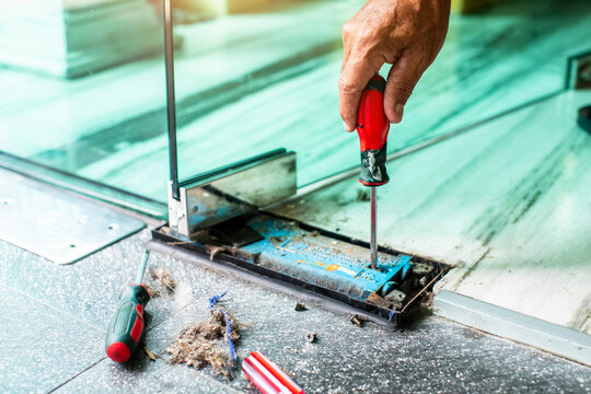 An interior decorator uses a screwdriver to adjust the angle of a swinging glass door.