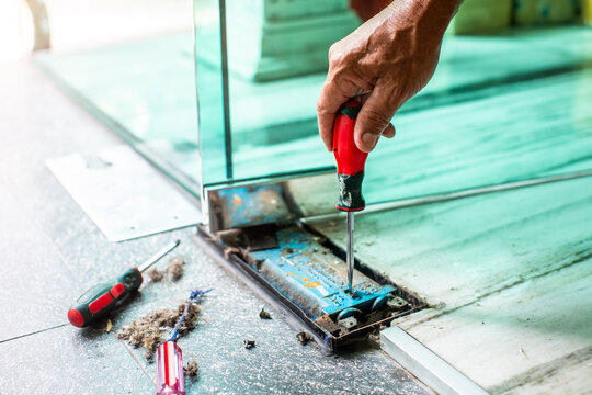 An interior decorator uses a screwdriver to adjust the angle of a swinging glass door.
