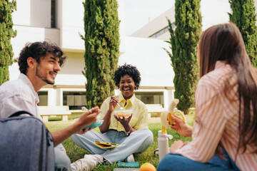 Multiethnic students eating and chatting at college campus. Focus on cheerful african female.