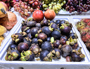 A vibrant market display featuring fresh fruits, with mangosteens prominently in the foreground alongside grapes, pomegranates, and rambutans.