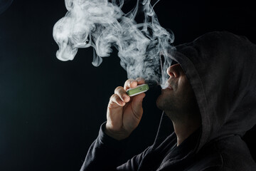a man smokes a vape electronic cigarette in black clothes on a dark background, close-up
