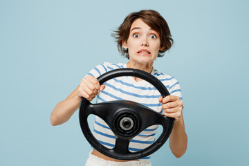 Young sad shocked woman she wears striped t-shirt casual clothes hold steering wheel driving car looking camera isolated on plain pastel light blue cyan background studio portrait. Lifestyle concept.