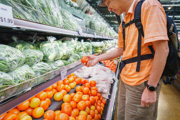 Man choosing fresh tomatoes at the supermarket. Customers buying food at grocery shops. California.