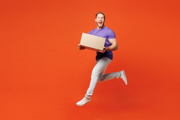 Full body young surprised shocked happy man he wearing purple t-shirt casual clothes holding cardboard box jump high hurry up isolated on red orange wall background studio portrait. Lifestyle concept.