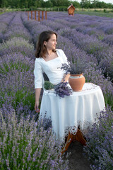 A young attractive woman in a white dress sits at a table in the middle of a lavender field	