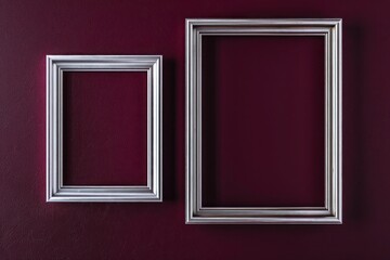 Avant-garde gallery mockup with two silver frames on a deep burgundy wall background.