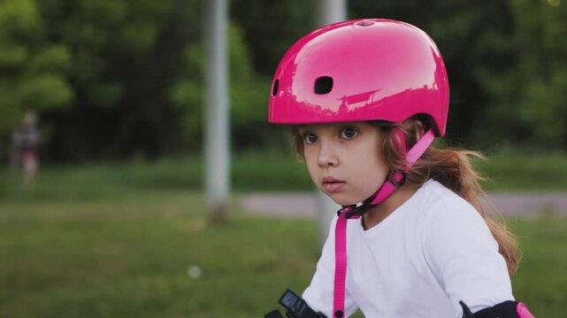 A portrait of a beautiful, blonde, focused girl riding a bicycle down the street in a pink helmet and pink elbow pads.