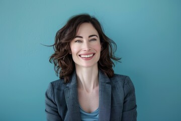 Fototapeta premium Portrait of a happy caucasian woman in her 30s dressed in a stylish blazer in front of soft blue background