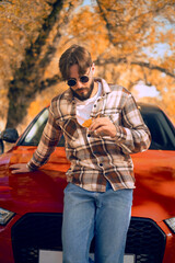 Man in plaid shirt standing by a car in an autumn park, promoting trips and excursions to nature