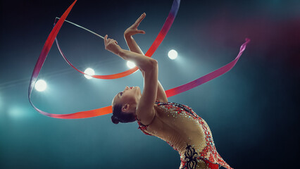 Elegant Female Gymnast in Stunning Backbend, Skillfully Twirling Vibrant Ribbon Under Bright...