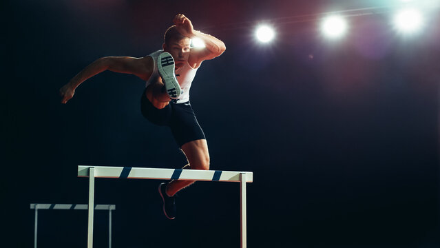 Male Athlete in Mid-air, Leaping Over Hurdle Under Bright Stadium Lights. Agility, Strength, and Determination in High-energy Track and Field Championship Event.