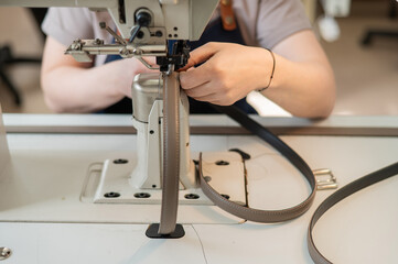 A woman tanner sews a leather belt on a sewing machine. Close-up of hands.