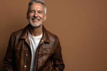 Obraz premium Portrait of a joyful caucasian man in his 40s sporting a classic leather jacket in front of soft brown background