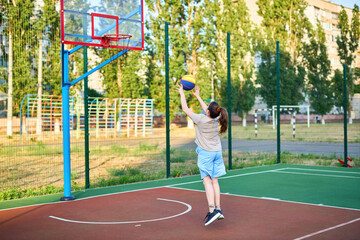 caucasian little basketball player jumps to throw the ball into the basket hoop