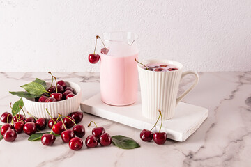 A delicious healthy dessert of a cherry smoothie in a white ceramic mug and a jug of smoothies on a white wooden stand among ripe cherries.