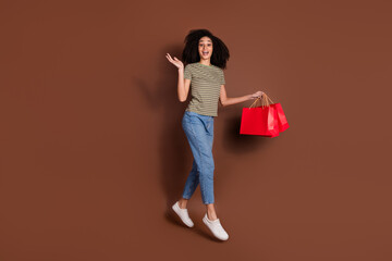 Full length photo of cheerful excited lady dressed khaki t-shirt jumping high rising bargains empty space isolated brown color background