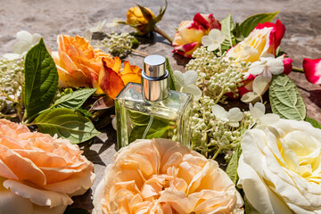 A beautiful bottle of cosmetic spray or perfume stands among colorful roses, flowers, leaves. Chic cosmetic background for product presentation.