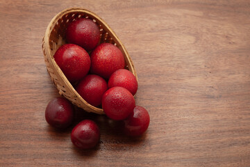 Top view of fresh Cherry Plum (Prunus cerasifera) fruits spilled out from a wooden basket, on a wooden background.