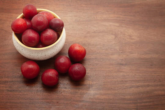 Top view of fresh Cherry Plum (Prunus cerasifera) fruits in a ceramic bowl, on a wooden background.