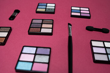 A set of multi-colored eyeshadow and brushes on a pink background. Eye makeup